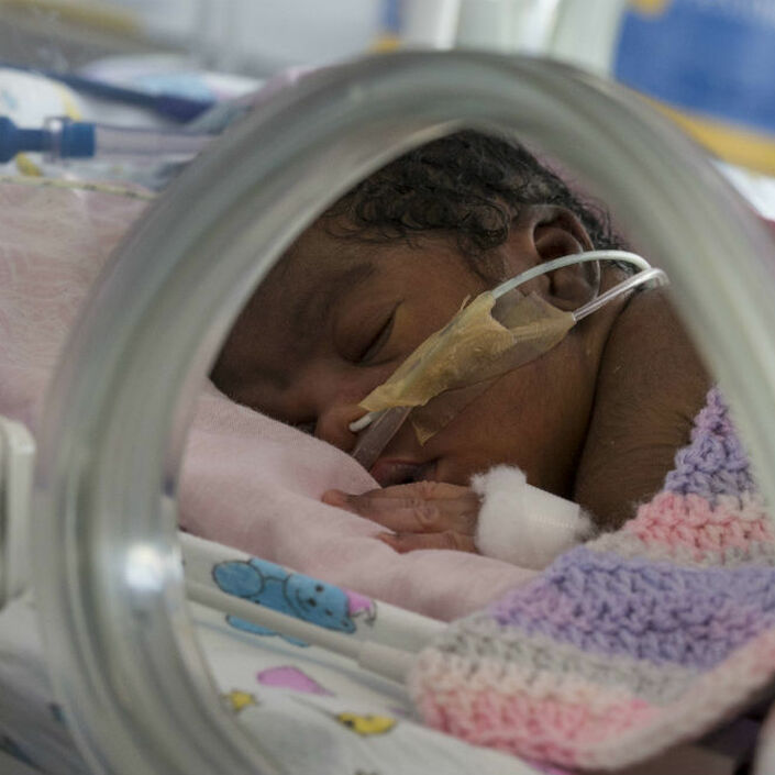 Baby covered in blanket attached to feeding tube sleeping peacefully in an incubator