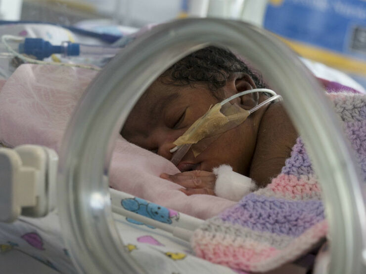 Baby covered in blanket attached to feeding tube sleeping peacefully in an incubator