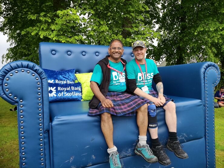 Two kiltwalk fundraisers wearing Bliss t-shirts and kilts sat on a extremely large sofa