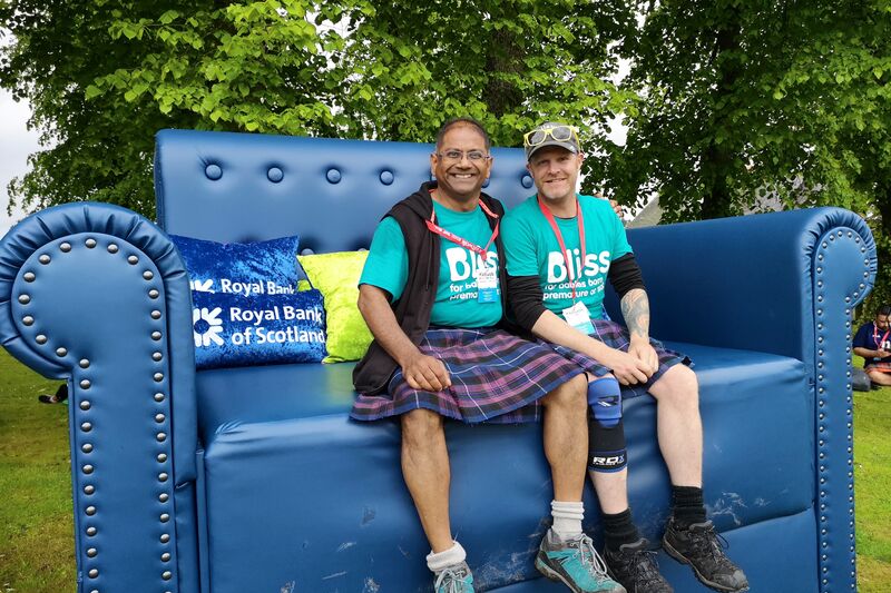 Two kiltwalk fundraisers wearing Bliss t-shirts and kilts sat on a extremely large sofa