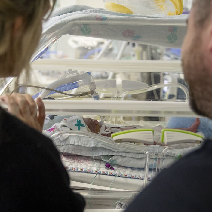 Two parents looking at their baby who is in an incubator