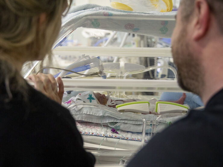 Two parents looking at their baby who is in an incubator