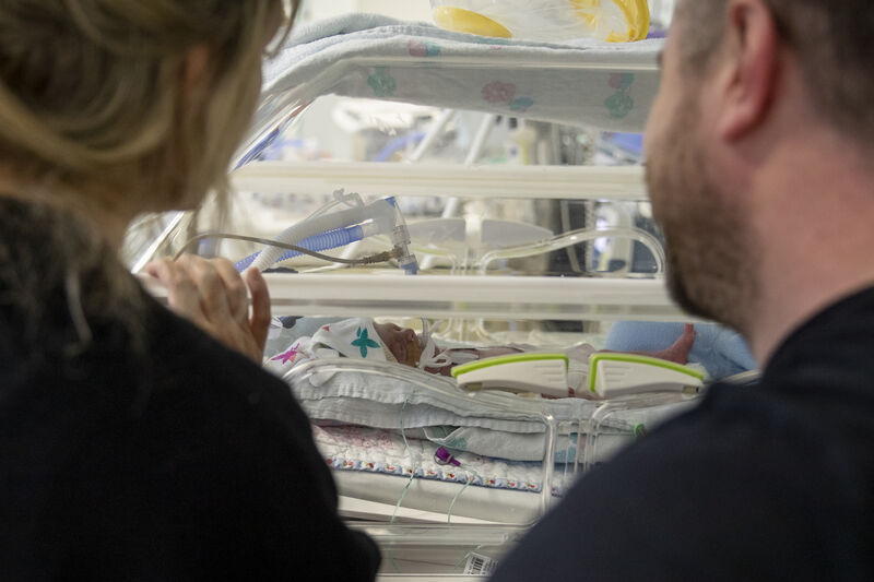 Two parents looking at their baby who is in an incubator