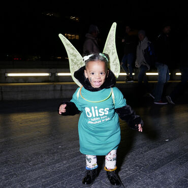 Young child wearing Bliss t-shirt, glowstick necklack and angel wings