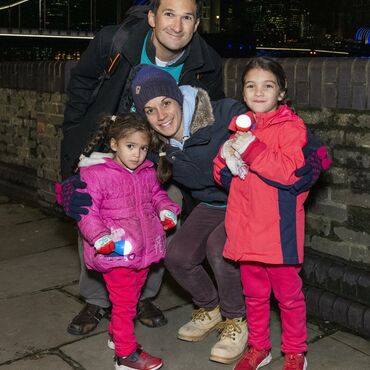 Dad, Mum and 2 children holding torches with Tower Bridge in the background at night.