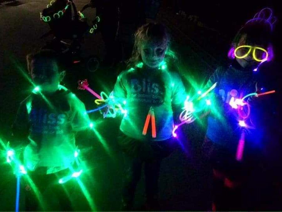 Darkness with 3 people wearing Bliss t-shirts lit up with glow sticks and lights