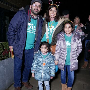 Family wearing warm coats, Bliss t-shirts and glow stick head bands and necklaces at a night time event