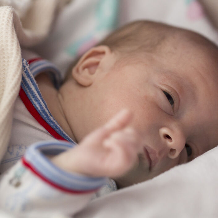 Baby lying in a cot covered in a wool blanket