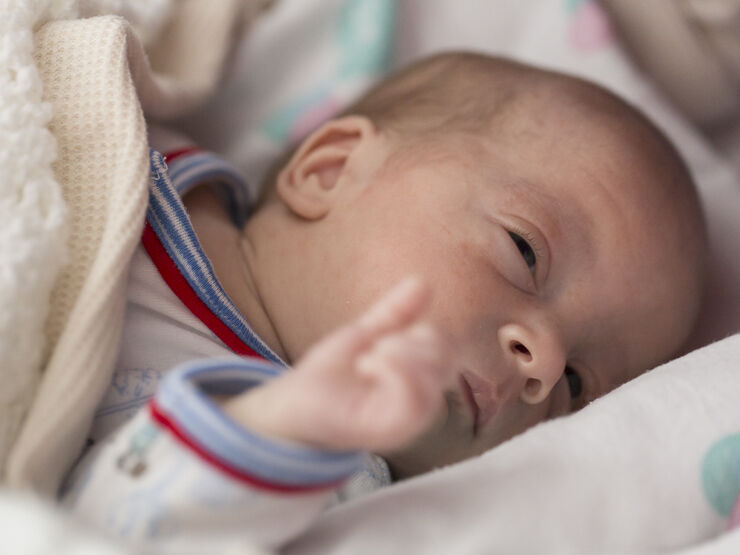 Baby lying in a cot covered in a wool blanket