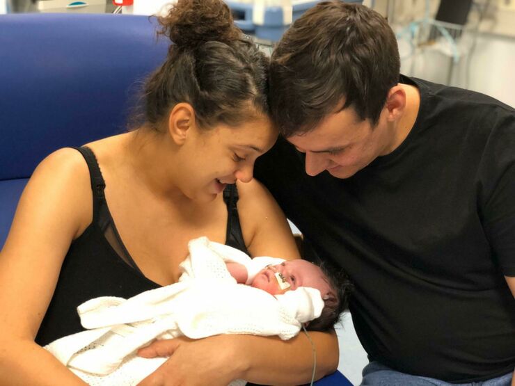 Mum sitting in chair in hospital holding baby with dad alongside looking at the baby