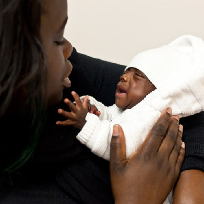 Mother holding and looking down at her baby who is reaching up towards her face.