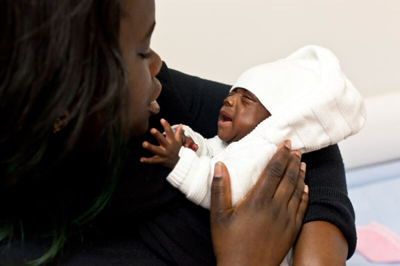 Mother holding and looking down at her baby who is reaching up towards her face.