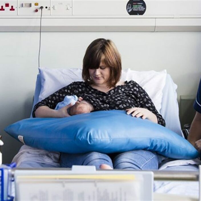 Mother sitting on a hospital bed breastfeeding her baby with a nurse nearby