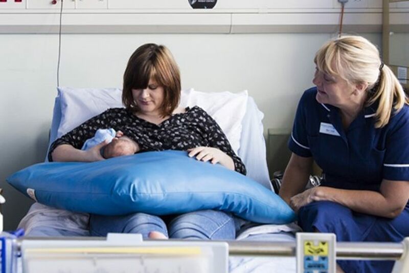 Mother sitting on a hospital bed breastfeeding her baby with a nurse nearby