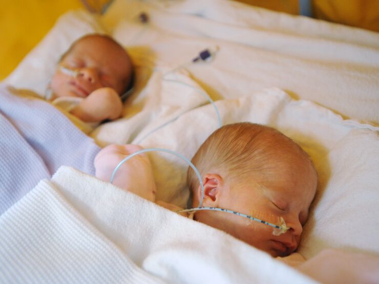 Two babies laying side by side wrapped in blankets and sleeping, with tubes attached to their nose