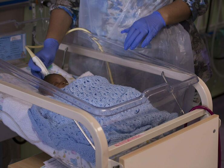 Healthcare professional with gloves on touching a baby's head with a small medical device