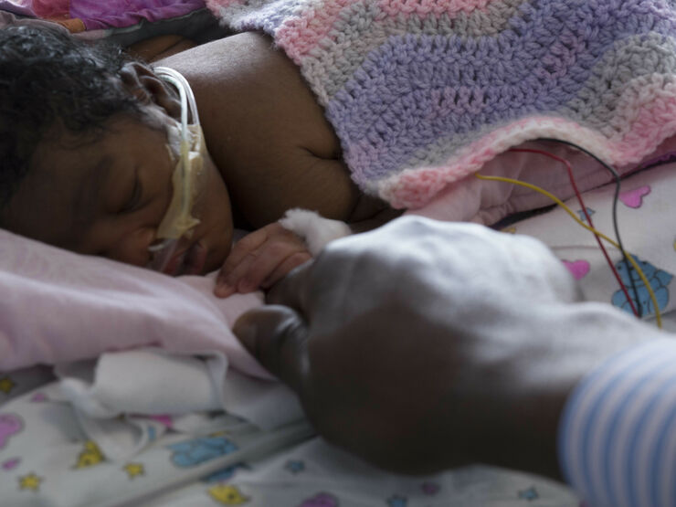 Baby with tubes in nose covered in a blanket holding their father's finger