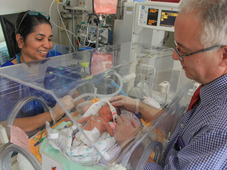 Doctor with his hands through an incubator looking after a baby while a nurse looks on smiling