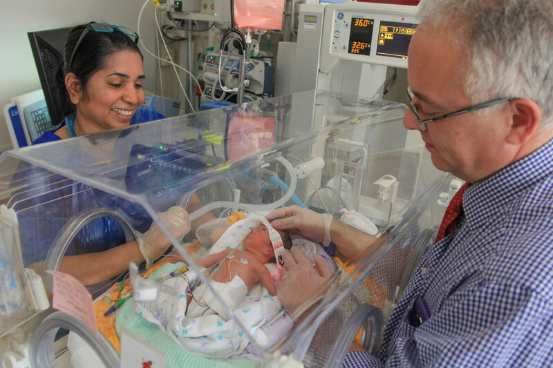 Doctor with his hands through an incubator looking after a baby while a nurse looks on smiling