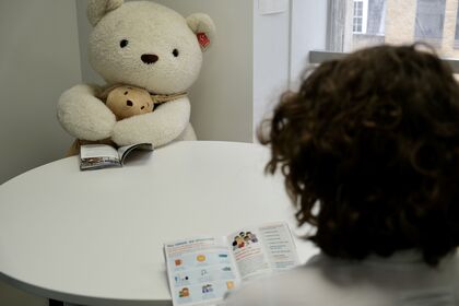 Person reading a leaflet sat across the table from a human-sized teddy bear