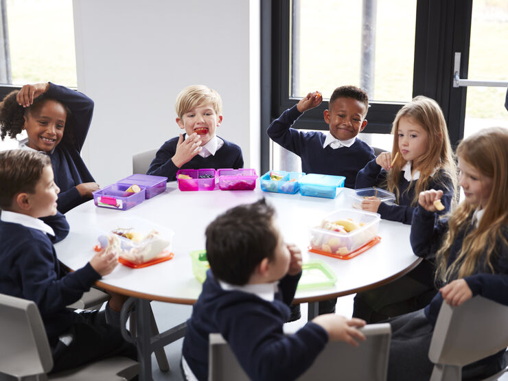 Group of primary school children sat at a round table having lunch and laughing