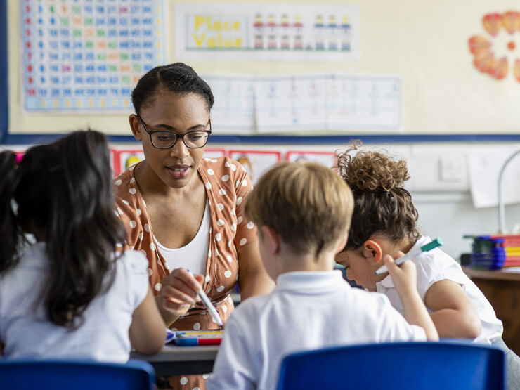 A teacher helping three primary school children with their work in a classroom