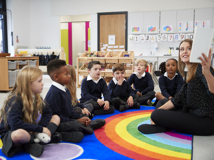 Primary school class sitting on the floor while teacher reads them a book