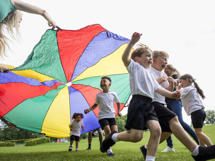 A group or children playing outside with a colourful parachute