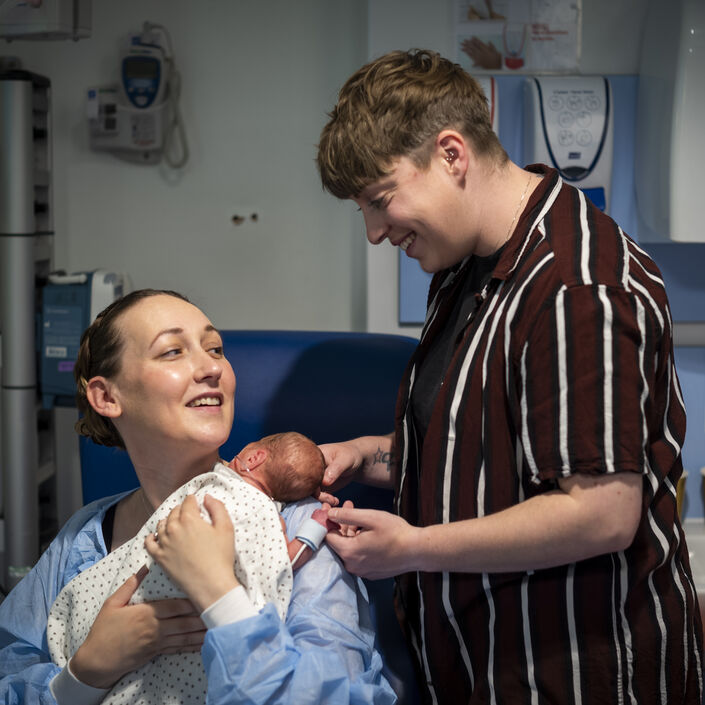 Mum holding premature baby on her chest while her partner holds baby's head and hand from behind