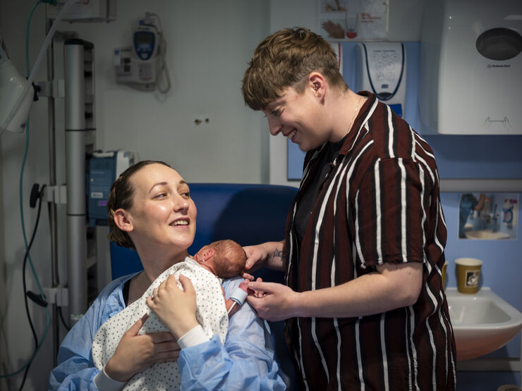 Mum holding premature baby on her chest while her partner holds baby's head and hand from behind
