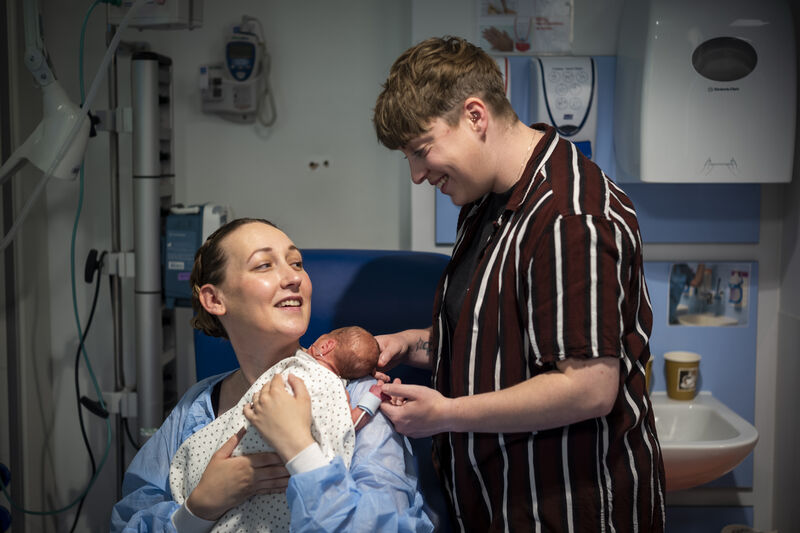 Mum holding premature baby on her chest while her partner holds baby's head and hand from behind
