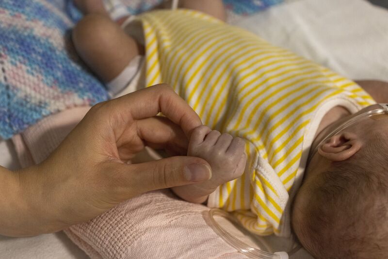 A parent holding their baby's hand while they lie in a bed