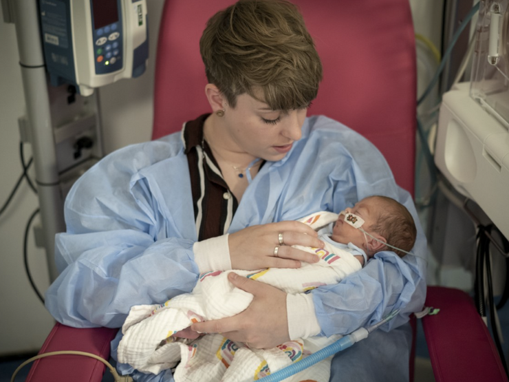Woman sat in a hospital chair holding her baby in her arms while looking down tenderly