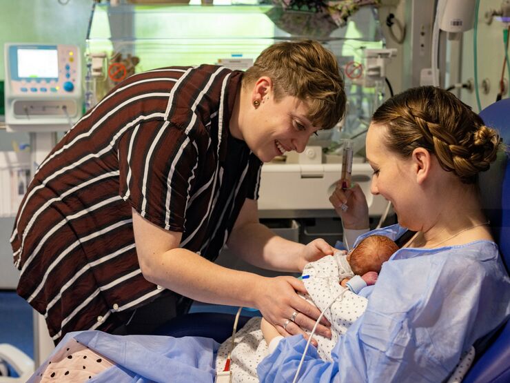 Woman holding baby on her chest in a hospital setting while her partner gently touches the baby's side