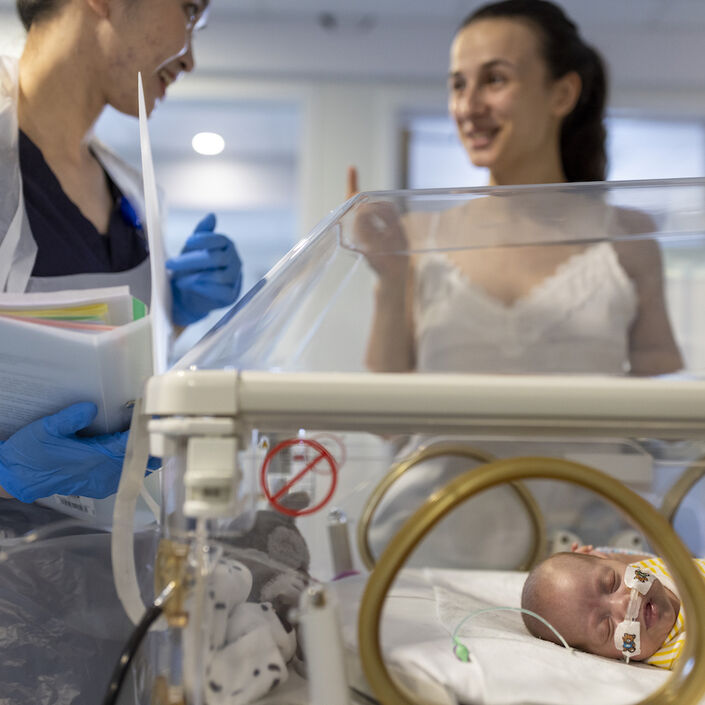 Mum and nurse talking in the background with a sleeping baby in an incubator in the foreground