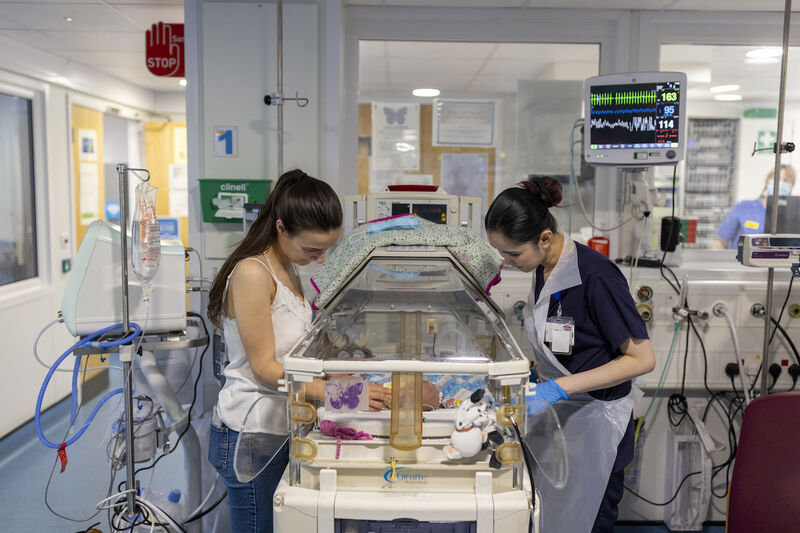 Mum and nurse standing over incubator looking at the baby