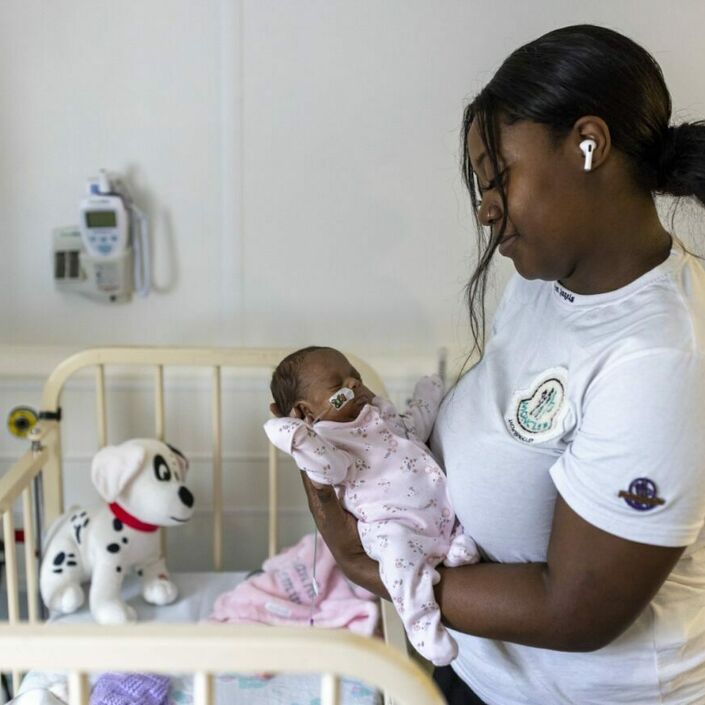 Smiling women of colour standing next to a cot holding their baby in their arms
