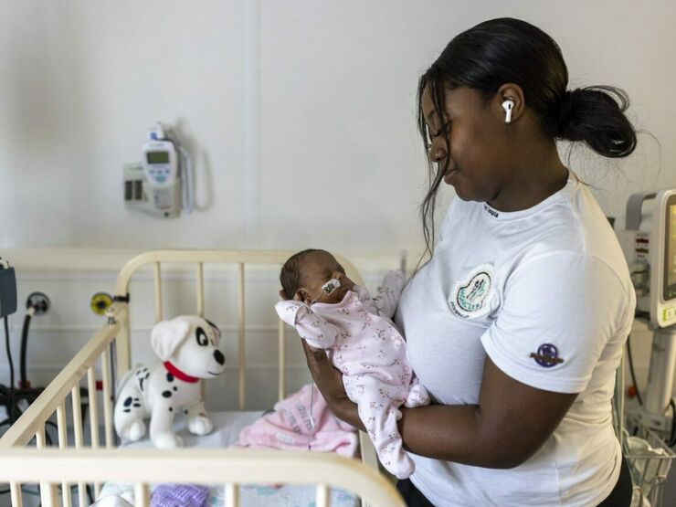 Smiling women of colour standing next to a cot holding their baby in their arms