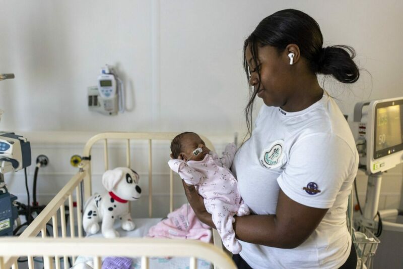 Smiling women of colour standing next to a cot holding their baby in their arms