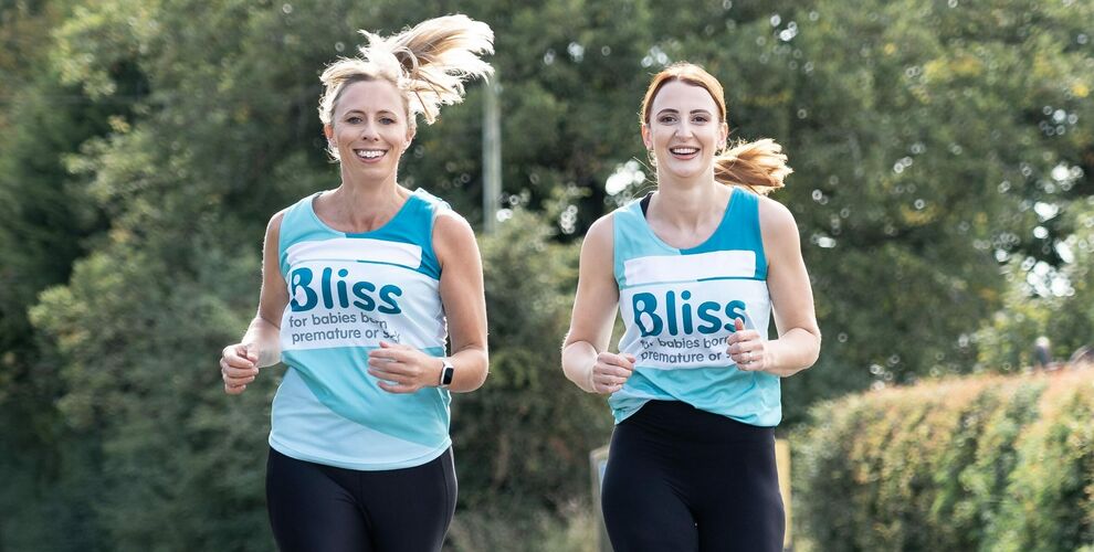 Two women running down the road together wearing Bliss running vests