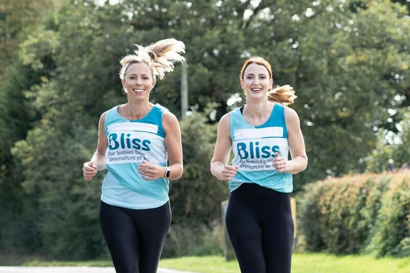 Two women running down the road together wearing Bliss running vests