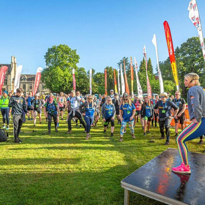 Lots of people at the start area for a walking event, warming up doing stretches