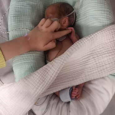 Baby in hospital with sibling's finger touching baby's hand