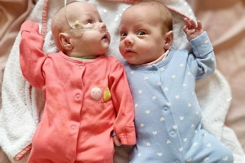 Twin babies wearing pyjamas lying on bed