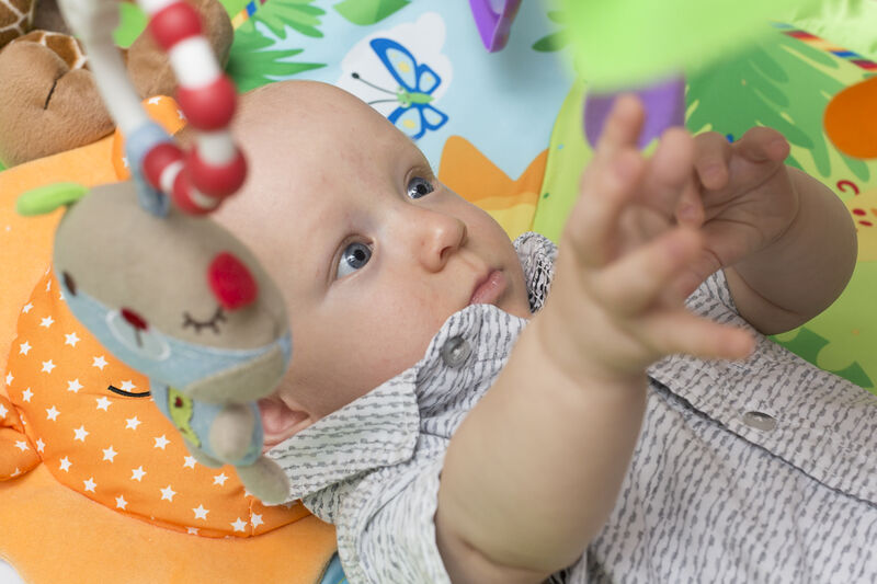 Baby lying on his back reaching up for a toy