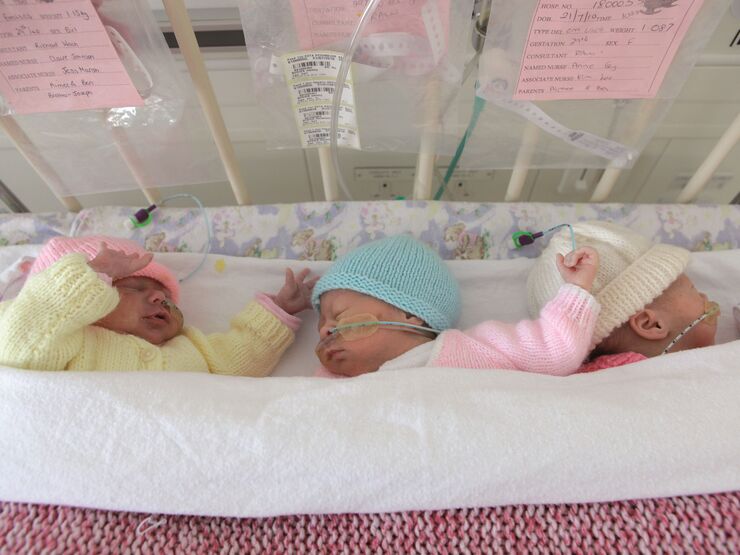 Triplets sleeping together in a cot. They are all attached to feeding tubes and wearing knitted hats.