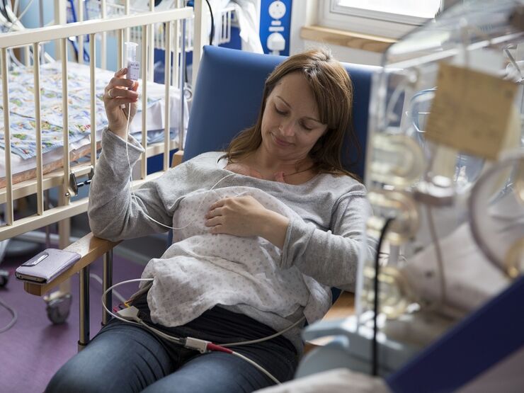 Mother in a hospital chair with her baby in her arms with tubes attached