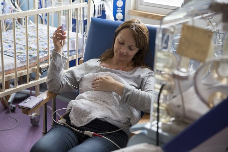 Mother in a hospital chair with her baby in her arms with tubes attached