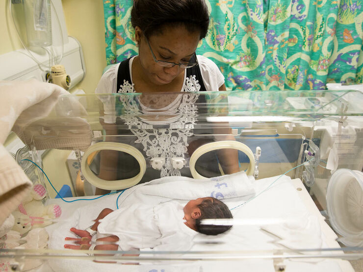 Mum in neonatal unit looking at her baby who is lying in a hospital cot