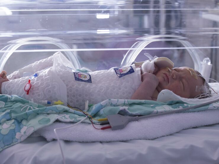 Baby in an incubator lying on a knitted blanket and wrapped in an insulated plastic layer